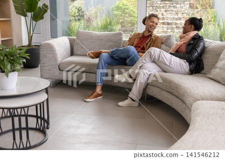 Diverse couple sitting on curved gray sofa in modern lounge, chatting near coffee table plants Diverse couple sitting on curved gray sofa in modern lounge, chatting near coffee table plants 141546212