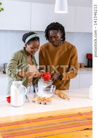 African American couple in casual clothes sifting flour with sifter and red cup at counter African American couple in casual clothes sifting flour with sifter and red cup at counter 141546213