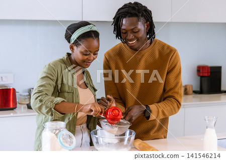African American couple preparing batter in bright home kitchen, sifting flour with metal sifter African American couple preparing batter in bright home kitchen, sifting flour with metal sifter 141546214