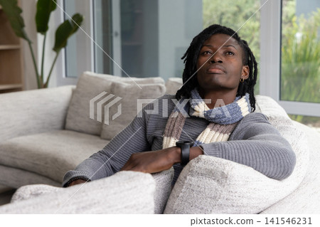 African American man reclining on light gray sofa, wearing knitted scarf and smartwatch, copy space African American man reclining on light gray sofa, wearing knitted scarf and smartwatch, copy space 141546231