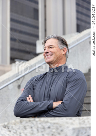Senior man standing on stairs near railing, crossing arms, smiling, looking left in zipup pullover 141546237