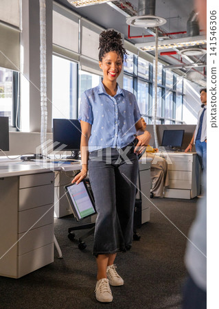 Diverse coworkers with African American woman leaning on desk holding tablet chart in office 141546306