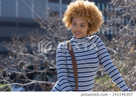 African American woman standing and smiling, wearing striped top and brown crossbody at urban plaza African American woman standing and smiling, wearing striped top and brown crossbody at urban plaza 141546307