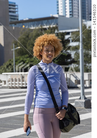 African American woman walking across plaza in sportswear carrying duffel and checking phone African American woman walking across plaza in sportswear carrying duffel and checking phone 141546310