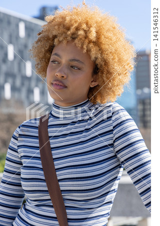 African American woman 20s leaning on concrete ledge in urban plaza, wearing striped top, brown bag African American woman 20s leaning on concrete ledge in urban plaza, wearing striped top, brown bag 141546312