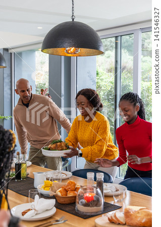 African American family carrying and serving roasted chicken at dining table with napkins, rolls African American family carrying and serving roasted chicken at dining table with napkins, rolls 141546327
