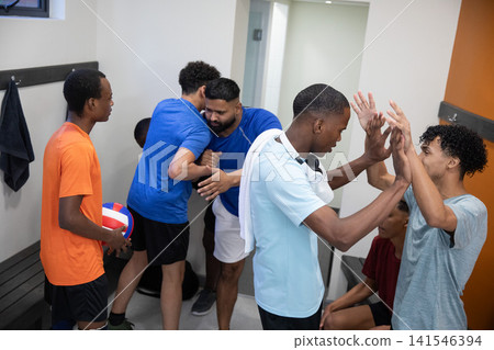 Diverse male teammates high-fiving in locker room wearing T-shirts with volleyball, copy space Diverse male teammates high-fiving in locker room wearing T-shirts with volleyball, copy space 141546394