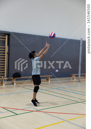 African American teen male jumping, reaching for red-white-blue volleyball on gym wearing kneepad African American teen male jumping, reaching for red-white-blue volleyball on gym wearing kneepad 141546500