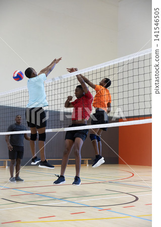 African American men jumping at net in gym, blocking and reaching for red white blue volleyball African American men jumping at net in gym, blocking and reaching for red white blue volleyball 141546505