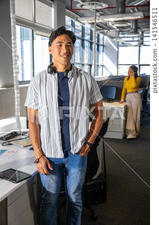 Diverse coworkers standing in office, Asian man wearing headphones, female speaking on smartphone Diverse coworkers standing in office, Asian man wearing headphones, female speaking on smartphone 141546511