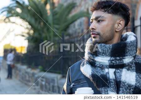 Man standing on city sidewalk holding white takeaway cup and wearing checkered scarf, copy space Man standing on city sidewalk holding white takeaway cup and wearing checkered scarf, copy space 141546519