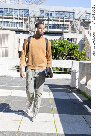 African American male late 20s walking on checkerboard plaza by modern building holding skateboard African American male late 20s walking on checkerboard plaza by modern building holding skateboard 141546523
