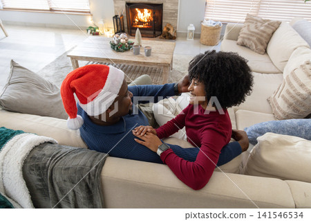 African American couple sitting closely on sectional sofa in living room, holding mugs by fireplace African American couple sitting closely on sectional sofa in living room, holding mugs by fireplace 141546534