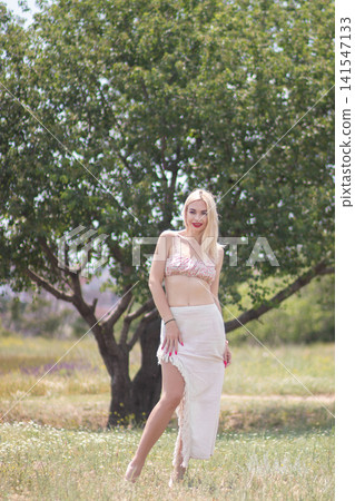 Full body outdoor portrait of one adult woman smiling while standing in a meadow near a tree. Fits summer fashion, happiness, beauty, and lifestyle projects. Full body outdoor portrait of one adult woman smiling while standing in a meadow near a tree. Fits summer fashion, happiness, beauty, and lifestyle projects. 141547133