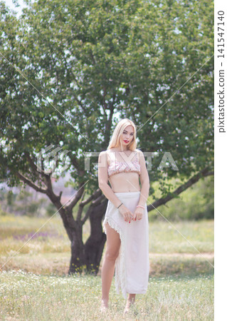 Full body portrait of one adult woman standing outdoors in a sunny meadow near a tree. Suitable for fashion, beauty, nature, and relaxed lifestyle content. Full body portrait of one adult woman standing outdoors in a sunny meadow near a tree. Suitable for fashion, beauty, nature, and relaxed lifestyle content. 141547140