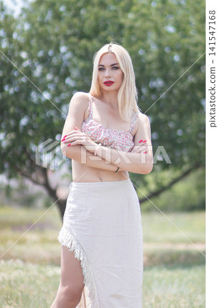 Fashion portrait of one adult woman standing in a sunny park with crossed arms and direct gaze. Ideal for summer style, beauty, confidence, and lifestyle themes. Fashion portrait of one adult woman standing in a sunny park with crossed arms and direct gaze. Ideal for summer style, beauty, confidence, and lifestyle themes. 141547168