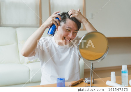 一位四十多歲的男子對著鏡子微笑,往頭上噴髮膠。 一位四十多歲的男子對著鏡子微笑,往頭上噴髮膠。 141547273
