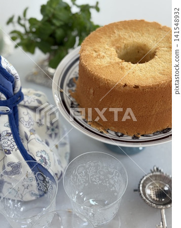 A scene featuring a white and blue tea cozy, green herbs, and homemade chiffon cake. A scene featuring a white and blue tea cozy, green herbs, and homemade chiffon cake. 141548932