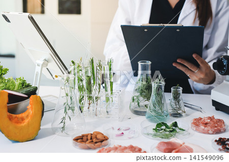 Scientists in lab coats work with plants in a modern lab, focusing on research and experimentation under bright, sterile conditions. Scientists in lab coats work with plants in a modern lab, focusing on research and experimentation under bright, sterile conditions. 141549096