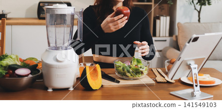 Woman preparing green smoothie in bright kitchen with fresh fruits and vegetables, healthy eating lifestyle moment in natural daylight Woman preparing green smoothie in bright kitchen with fresh fruits and vegetables, healthy eating lifestyle moment in natural daylight 141549103
