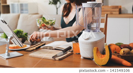 Woman preparing green smoothie in bright kitchen with fresh fruits and vegetables, healthy eating lifestyle moment in natural daylight Woman preparing green smoothie in bright kitchen with fresh fruits and vegetables, healthy eating lifestyle moment in natural daylight 141549106