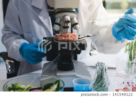 Scientists in lab coats work with plants in a modern lab, focusing on research and experimentation under bright, sterile conditions. Scientists in lab coats work with plants in a modern lab, focusing on research and experimentation under bright, sterile conditions. 141549122