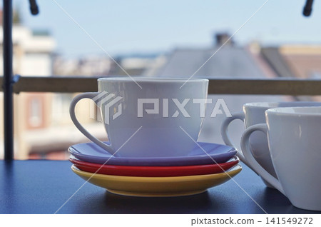 A white ceramic cup sits on stacked colorful saucers while another cup appears at the edge of the frame. The scene symbolizes companionship, shared conversation, and warmth in everyday home life 141549272