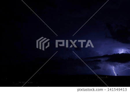 A narrow lightning bolt appears below layered storm clouds in a nearly black night sky. Minimal nocturnal scene symbolizes uncertainty, tension, and sudden natural energy. A narrow lightning bolt appears below layered storm clouds in a nearly black night sky. Minimal nocturnal scene symbolizes uncertainty, tension, and sudden natural energy. 141549413