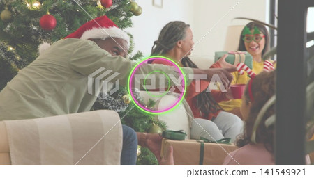 Passing gift man wearing Santa hat leaning in living room, family by decorated tree holding candy Passing gift man wearing Santa hat leaning in living room, family by decorated tree holding candy 141549921