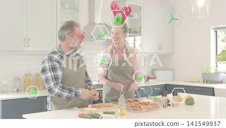 Chopping senior couple wearing green aprons slicing vegetables on kitchen island, with AR overlays Chopping senior couple wearing green aprons slicing vegetables on kitchen island, with AR overlays 141549937