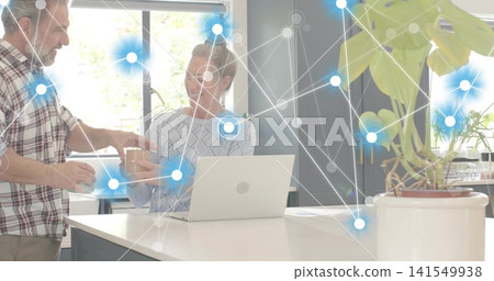 Handing man giving cup to woman using silver laptop at kitchen island, plaid shirt, network overlay Handing man giving cup to woman using silver laptop at kitchen island, plaid shirt, network overlay 141549938