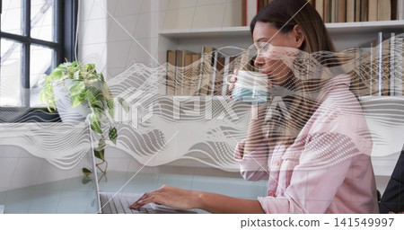 Working mid-adult-woman in light-pink shirt typing on laptop while sipping mug at home with window Working mid-adult-woman in light-pink shirt typing on laptop while sipping mug at home with window 141549997