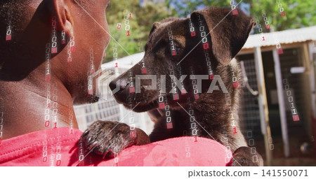 Holding dark puppy, man wearing red shirt cradling against shoulder in kennel with binary overlay Holding dark puppy, man wearing red shirt cradling against shoulder in kennel with binary overlay 141550071