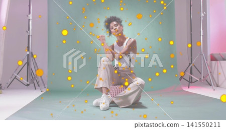 Sitting model wearing white top beige pants suspenders at studio, teal backdrop, pouf, lights bokeh Sitting model wearing white top beige pants suspenders at studio, teal backdrop, pouf, lights bokeh 141550211