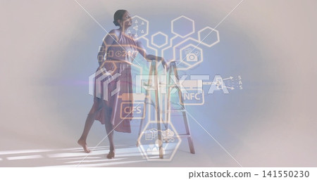 Posing Indian model holding ladder in studio, wearing sleeveless mauve dress barefoot, showing HUD 141550230