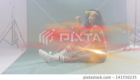 Posing model wearing visor and orange swimsuit on teal backdrop, holding prop with nebula overlay 141550235