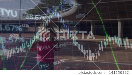 Walking woman in pink tee and jeans adjusting hair through urban plaza, showing financial charts 141550322