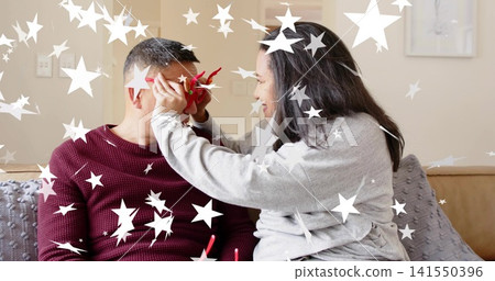 Holding red flower, couple wearing gray and burgundy sitting on beige couch in living room 141550396