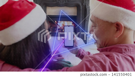 Sitting couple wearing Santa hats holding smartphone showing blank screen in living room, fireplace Sitting couple wearing Santa hats holding smartphone showing blank screen in living room, fireplace 141550401