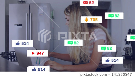 Working woman in striped tee typing on laptop, holding chart at kitchen counter with social alerts Working woman in striped tee typing on laptop, holding chart at kitchen counter with social alerts 141550547
