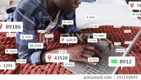 Typing man in plaid shirt, white tee reclining in bed with laptop, red throw, notifications Typing man in plaid shirt, white tee reclining in bed with laptop, red throw, notifications 141550645
