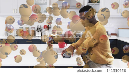 Man in mustard sweater typing on laptop, checking phone at kitchen island, emoji faces, copy space Man in mustard sweater typing on laptop, checking phone at kitchen island, emoji faces, copy space 141550658