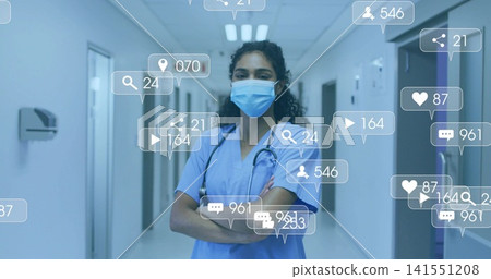 Standing nurse crossing arms in blue scrubs and mask at hospital hall, stethoscope and social icons Standing nurse crossing arms in blue scrubs and mask at hospital hall, stethoscope and social icons 141551208