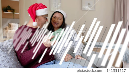 Showing couple sitting left of center on living room sofa, sharing smartphone, wearing Santa hats Showing couple sitting left of center on living room sofa, sharing smartphone, wearing Santa hats 141551317