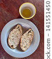 Freshly baked golden brown sourdough bread slice with crispy crust and chewy soft crumb, served with extra virgin olive oil in a small ceramic bowl on a rustic wooden table. 141551450