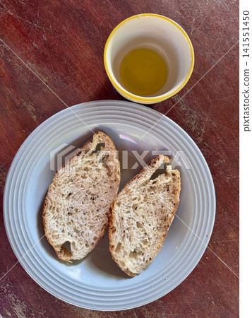 Freshly baked golden brown sourdough bread slice with crispy crust and chewy soft crumb, served with extra virgin olive oil in a small ceramic bowl on a rustic wooden table. Freshly baked golden brown sourdough bread slice with crispy crust and chewy soft crumb, served with extra virgin olive oil in a small ceramic bowl on a rustic wooden table. 141551450