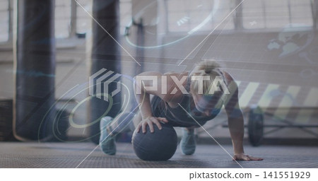 Performing mid-adult woman doing medicine-ball push-up at gym, wearing dark athletic gear, HUD Performing mid-adult woman doing medicine-ball push-up at gym, wearing dark athletic gear, HUD 141551929