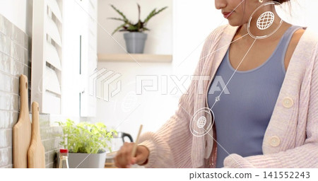 Stirring mid-adult woman in blue tank, pink cardigan at counter with herb, red bottle, copy space Stirring mid-adult woman in blue tank, pink cardigan at counter with herb, red bottle, copy space 141552243