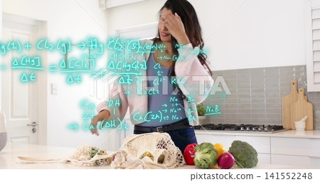 Gesturing woman studying produce at kitchen island wearing pink cardigan with turquoise overlay Gesturing woman studying produce at kitchen island wearing pink cardigan with turquoise overlay 141552248