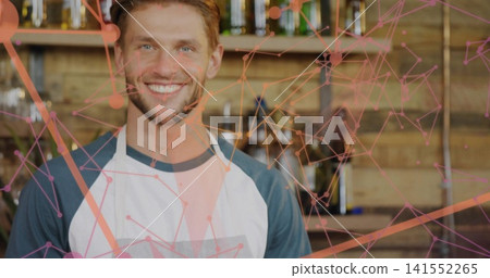 Smiling male barista wearing apron and raglan shirt, standing behind bar with pink orange overlay Smiling male barista wearing apron and raglan shirt, standing behind bar with pink orange overlay 141552265